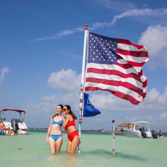 Two girls standing in the water at the Islamorada Sand Bar with an American Flag behind them.