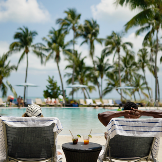 A couple sits in chaise lounges by the pool.