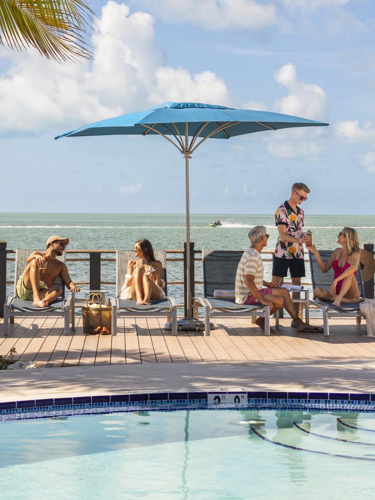 People on lounge chairs by the pool with the ocean in the background