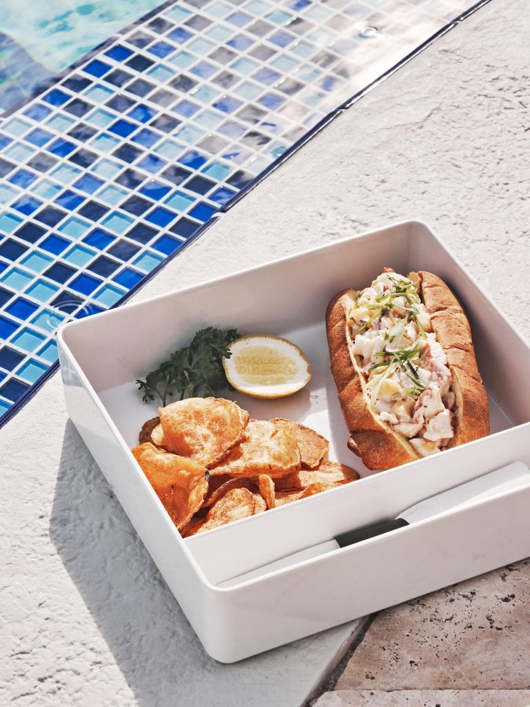 A cocktail, sandwich and chips shown next to a pool