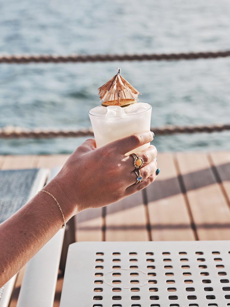 Hand holding a drink in front of the ocean