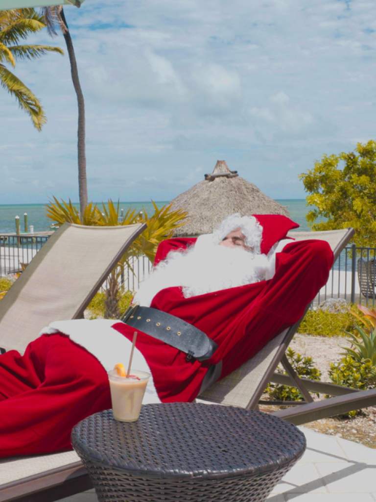 Santa laying on a chaise lounge by the pool.