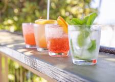 four cocktails on a railing with the ocean in the background