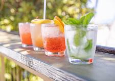 four cocktails on a railing with the ocean in the background